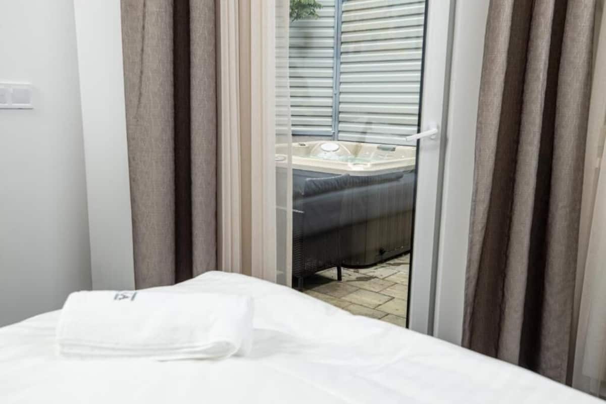 A hotel room with a bed, a window with blinds, and a view of an outdoor area with a hot tub.
