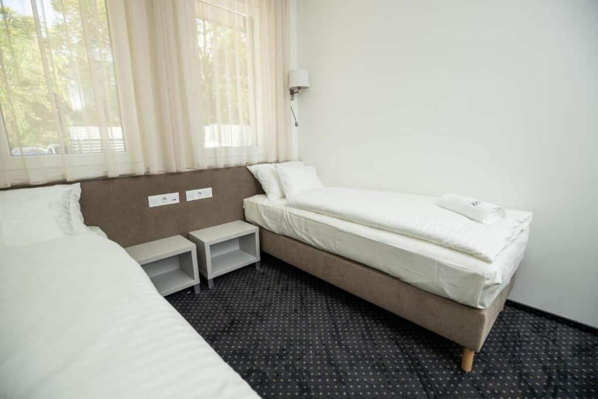 A hotel room with a single bed, a bedside table, a small shelf, and a window with curtains.