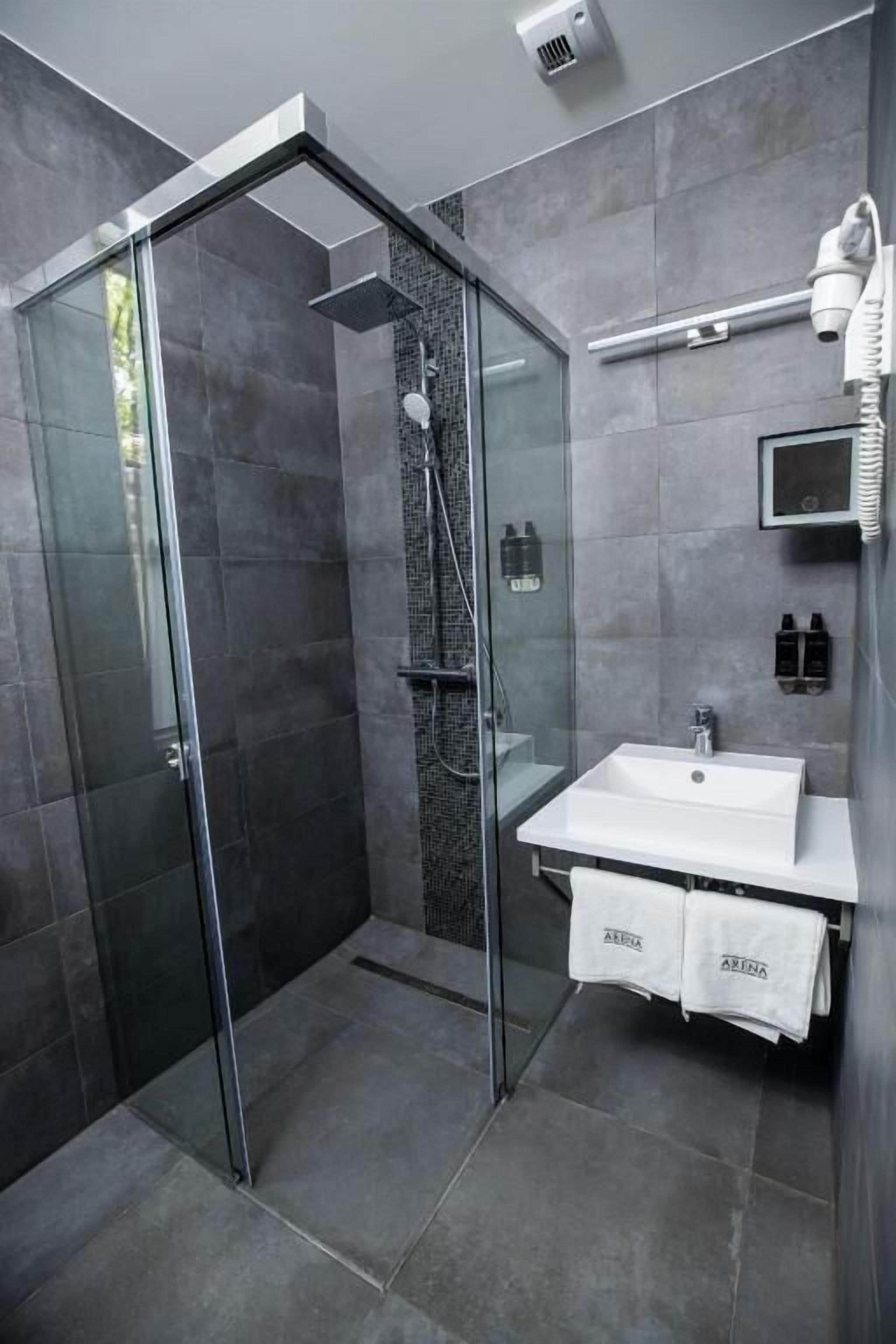 A modern bathroom with a glass-enclosed shower, a white sink, and a towel rack.