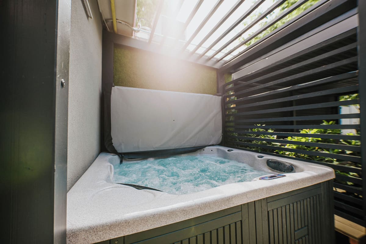 A hot tub with a white cover, surrounded by a wooden deck and metal blinds.