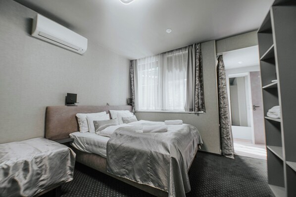Una habitación de hotel con cama, mesita de noche, aire acondicionado, ventana con cortinas y armario.