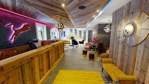 A modern lobby with wooden paneling, a reception desk, seating areas, and a large wall clock. - Hotel Panther'A (Saalbach)