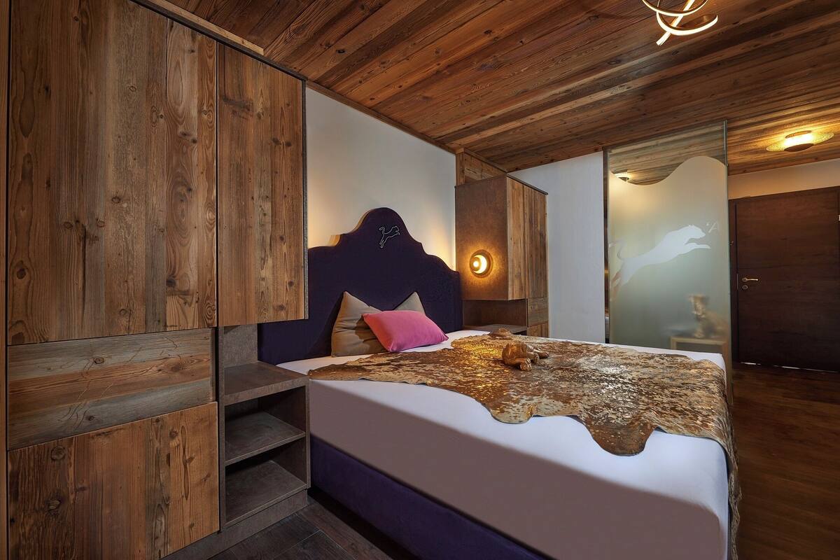 A bedroom with a wooden ceiling, a bed with a unique headboard, and a nightstand.