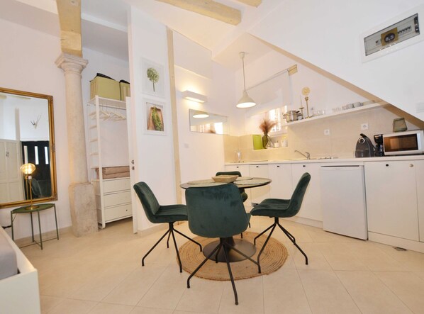 A modern kitchen with white cabinets, a dining area with a round table and green chairs, and a large mirror on the left.