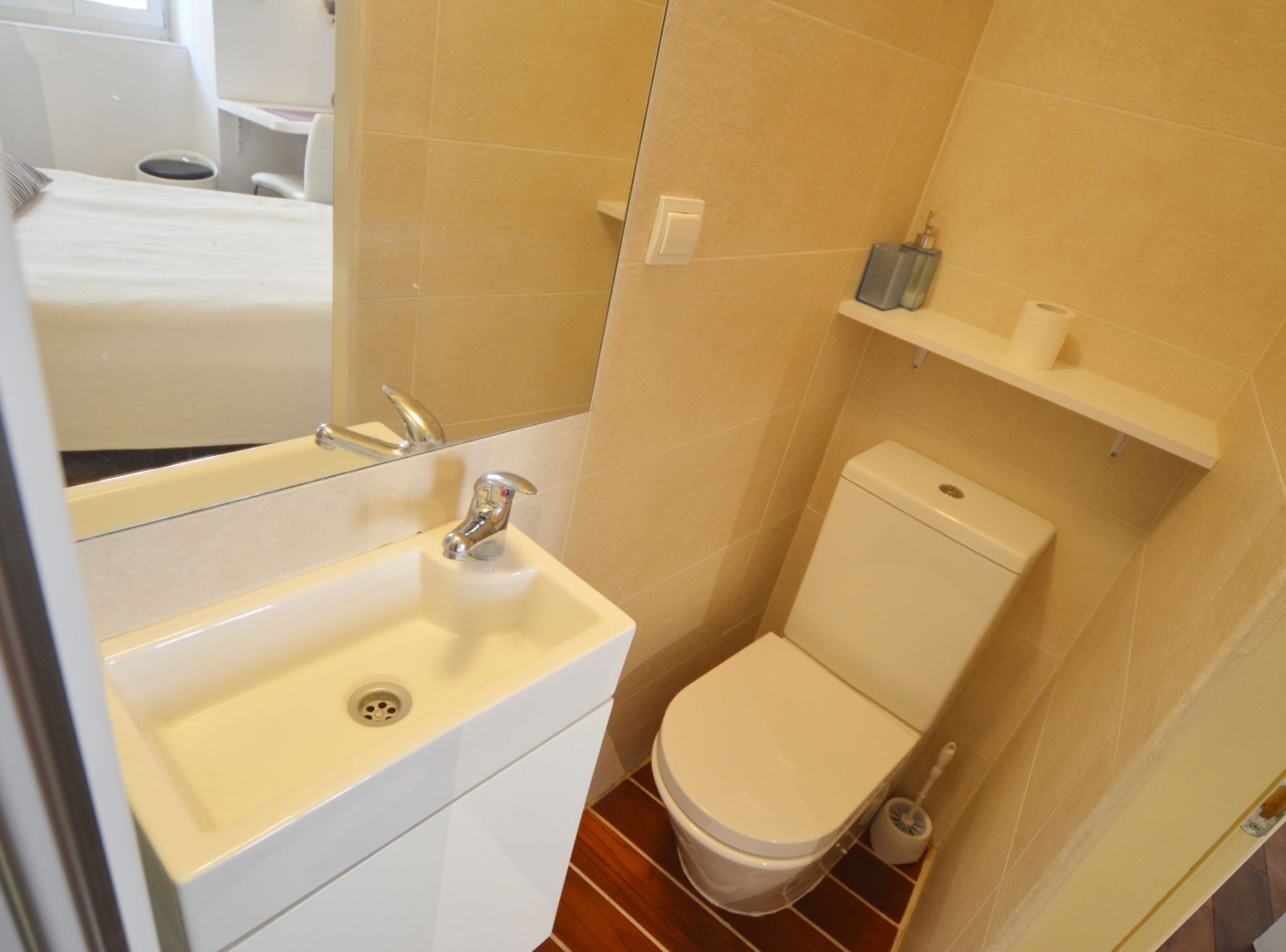 Een kleine badkamer met een wit wastafel, toilet en een plank met toiletartikelen.