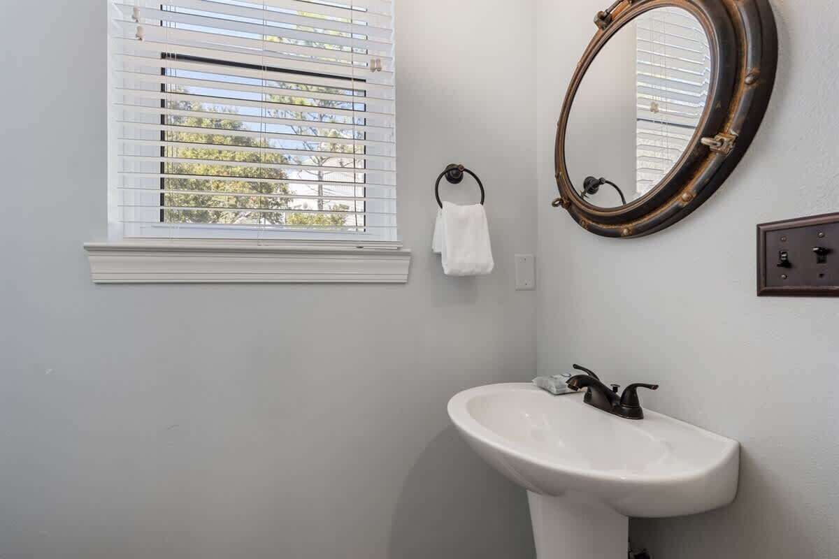 A bathroom with a white sink, a round mirror with a dark frame, a towel rack, and a window with blinds.