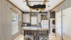 Eine Küche mit Holzbalken, einer hängenden Fischskulptur, einer Mittelinsel und eingebauten Geräten.