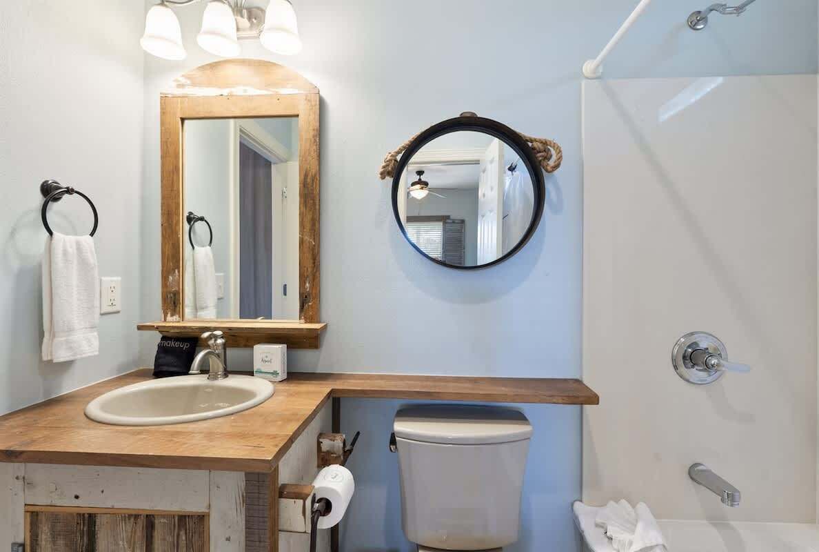 A bathroom with a wooden vanity, a large mirror, a round mirror, a toilet, and a shower area.