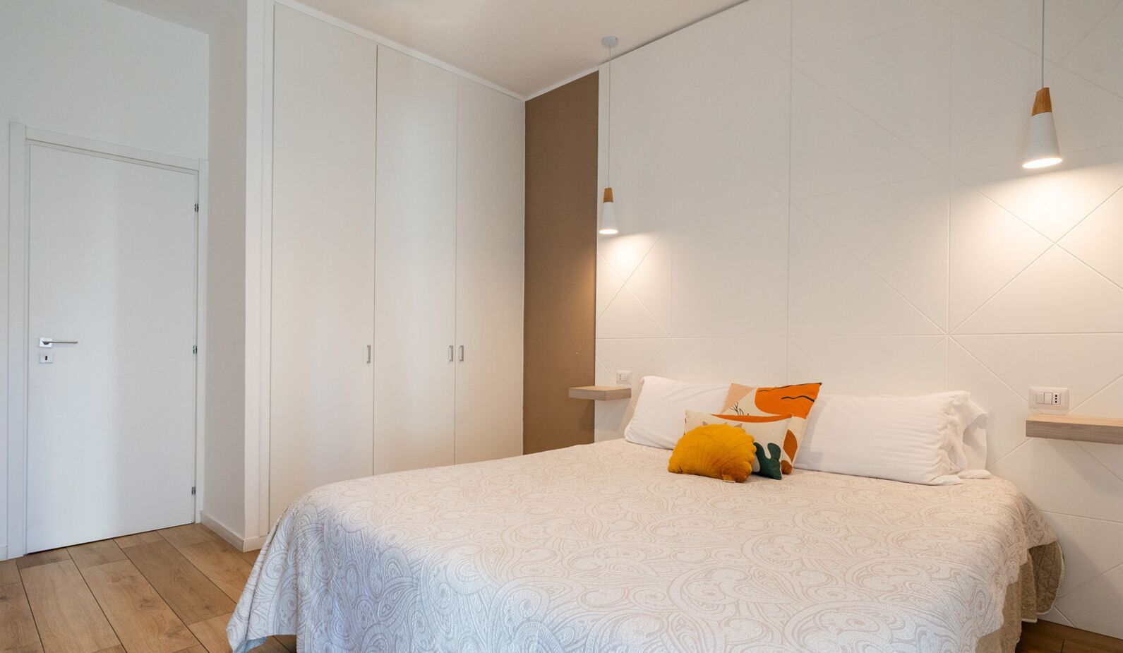 A bedroom with a bed, white walls, a wardrobe, and a bedside table.