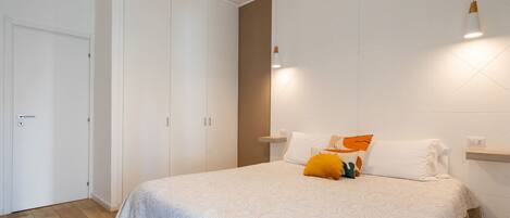 A bedroom with a bed, white walls, a wardrobe, and a bedside table.