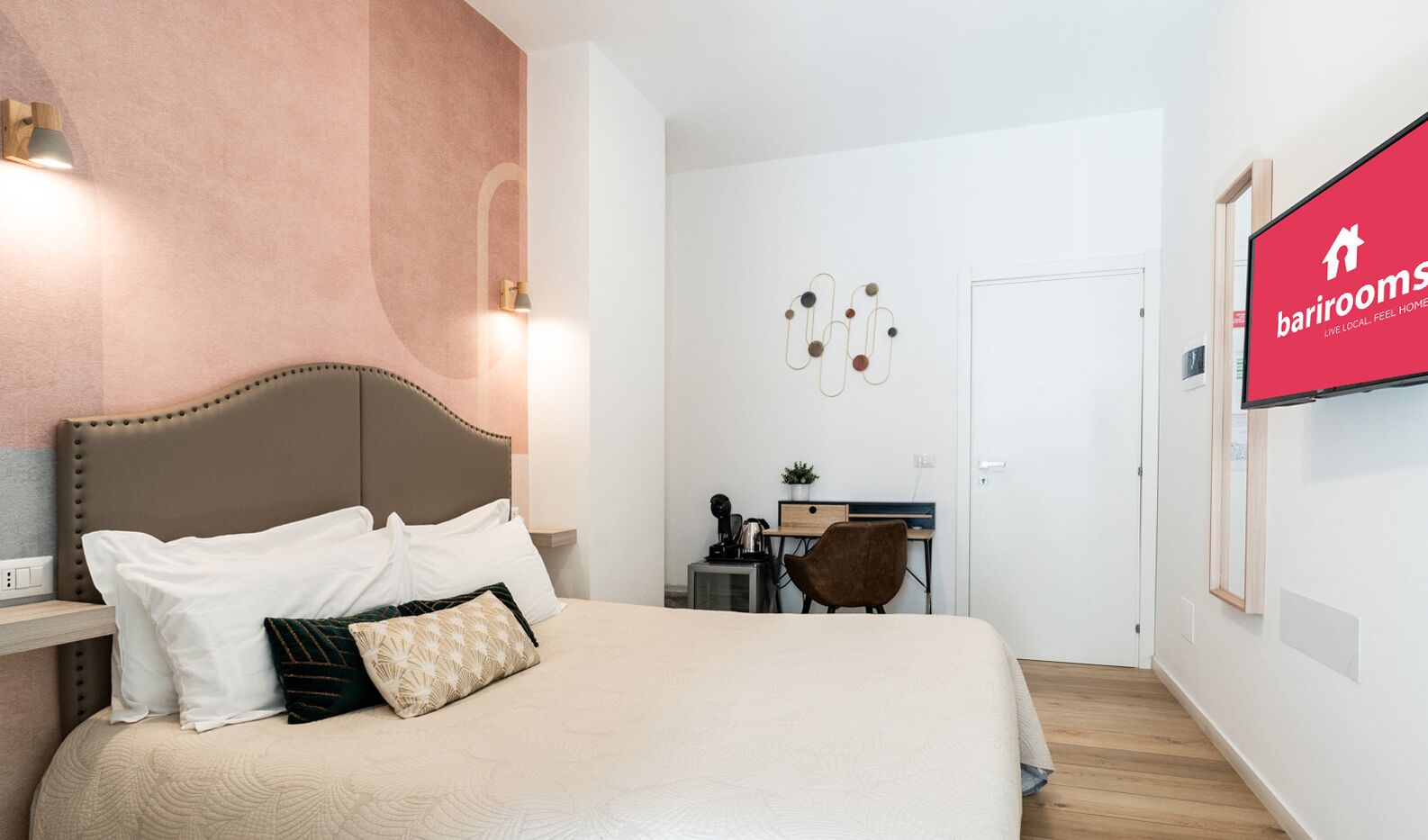 Una camera d'albergo con un letto grande, una scrivania e una TV appesa al muro.