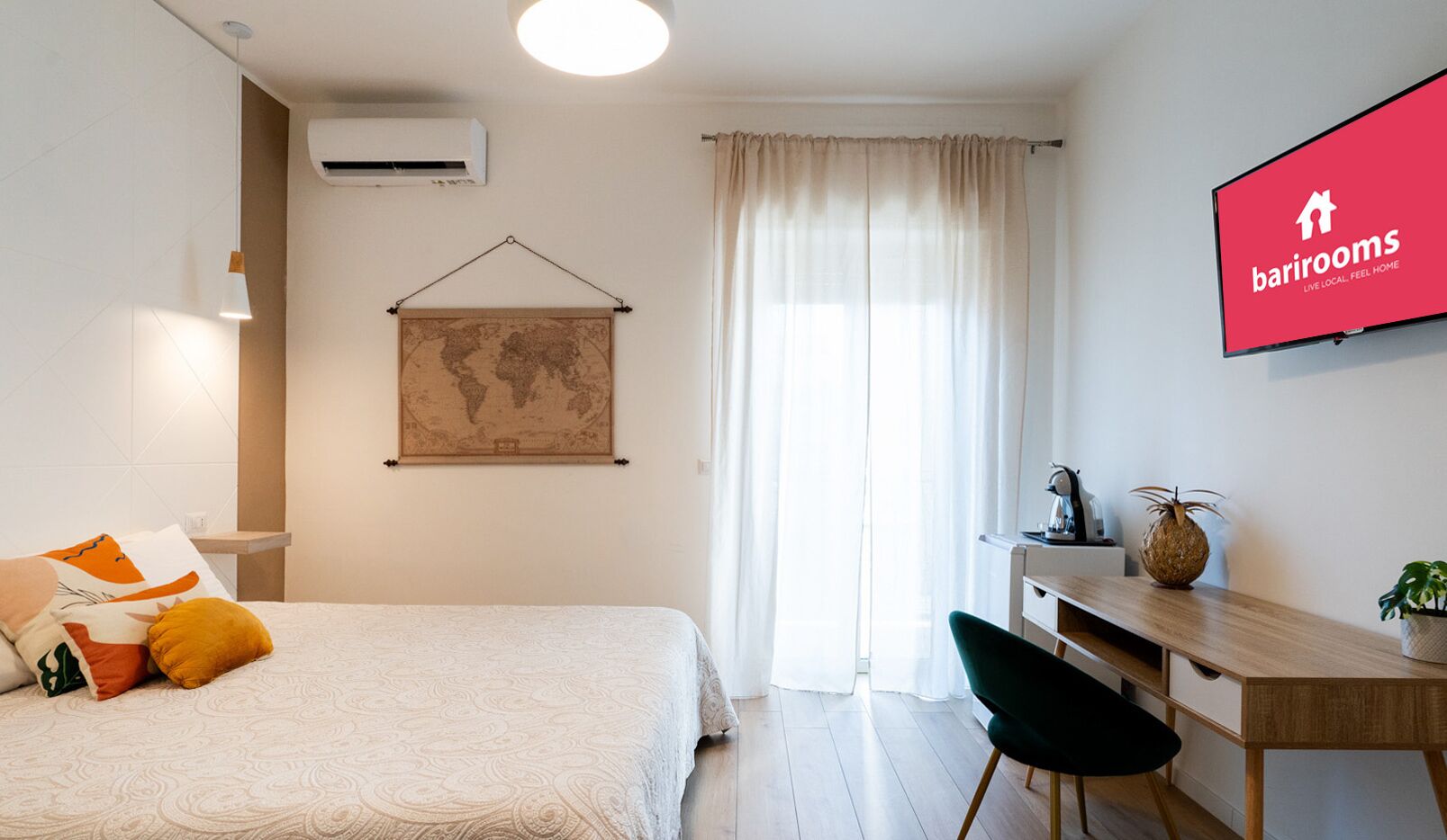 Une chambre d’hôtel équipée d’un lit, d’un bureau, d’une chaise, d’une carte du monde et d’un téléviseur diffusant l’émission « Barrirooms ».