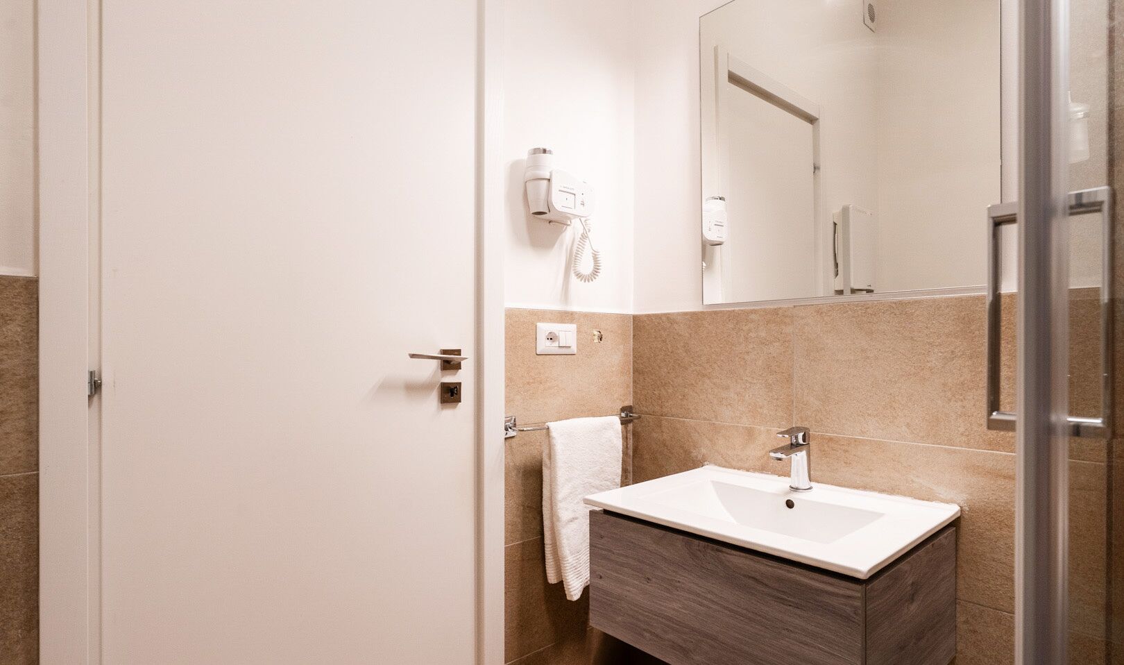 A modern bathroom with a white sink, a mirror, and a towel hanging on the wall.