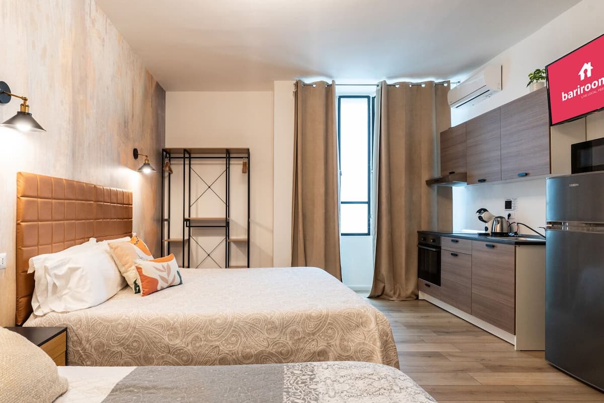 Ein kleines Hotelzimmer mit Bett, Nachttischen, einer kleinen Küchenzeile und Blick auf die Stadt.