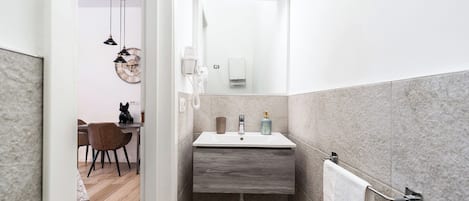 Un baño estrecho con un lavamanos blanco, un perchero y un espejo.