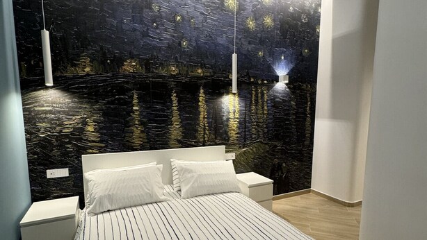 Un dormitorio con cama, mesitas de noche y un mural en la pared.