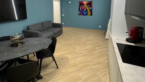 A modern kitchen with a dining area, a flat-screen TV, and a colorful abstract painting on the wall.