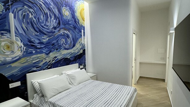 A modern bedroom with a bed, bedside tables, and a large wall mural.