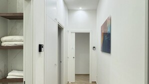 A modern, well-lit hallway with a wooden floor, white walls, and a door leading to another room.