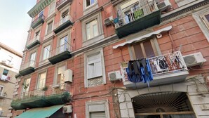 A multi-story building with balconies, air conditioning units, and a green awning.