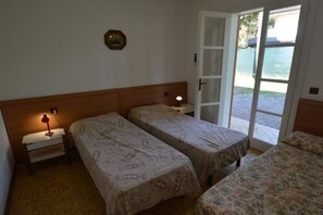 A room with two beds, a nightstand with a lamp, a door leading to an outdoor area, and a wall-mounted picture. - Comfy Beachside Vacation Home With Patio and Garden (Lignano Sabbiadoro)