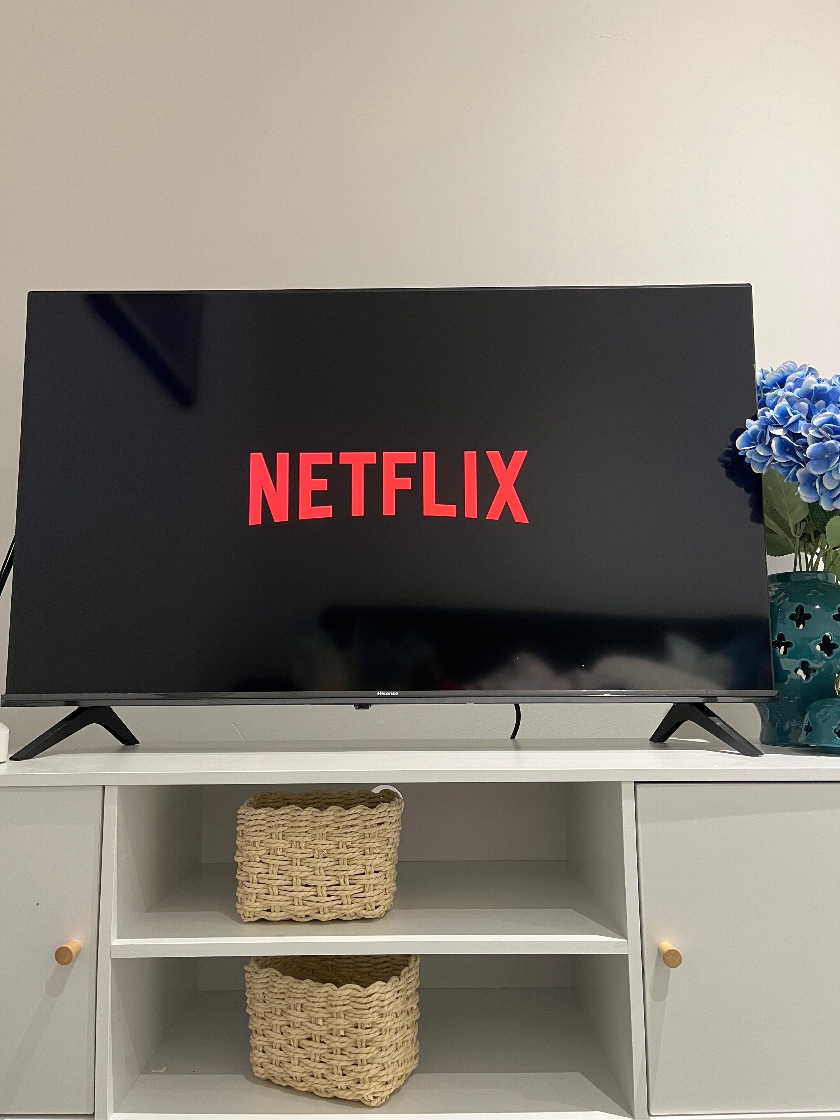 Un téléviseur à écran plat orné du logo Netflix, posé sur un meuble blanc, avec deux paniers en osier placés en dessous.