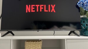 Et fladskærms-tv med Netflix-logoet på skærmen, placeret på et hvidt skab med to fletkurve nedenunder.