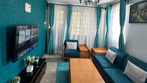 Un salon moderne avec des murs de couleur turquoise, un téléviseur à écran plat, une table basse en bois, des canapés turquoise et un lustre.
