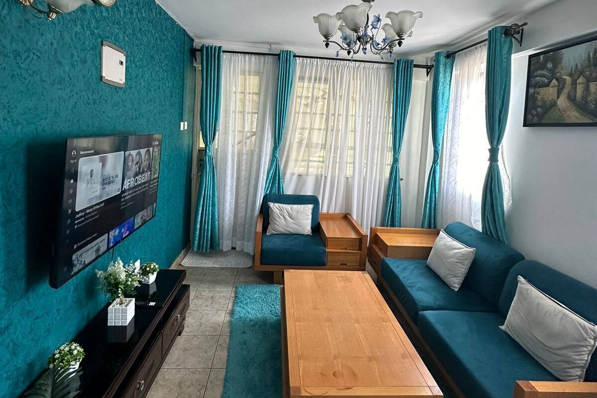 Un salon moderne avec des murs de couleur turquoise, un téléviseur à écran plat, une table basse en bois, des canapés turquoise et un lustre.