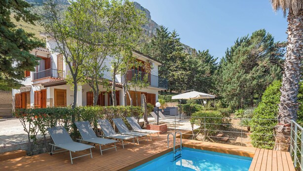 Ein Poolbereich mit Liegestühlen, einer Holzterrasse und einem Gebäude mit Balkonen.