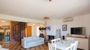 A spacious living area with a white sofa, a dining table with white chairs, a fireplace, and a TV mounted on the wall. - Villa Hybiscus with Pool in Castellammare del Golfo, Fraginesi, Scopello (Castellammare del Golfo)