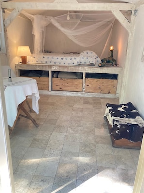 A small, cozy room with a bed, a bedside lamp, a table with a tablecloth, and a cowhide rug.