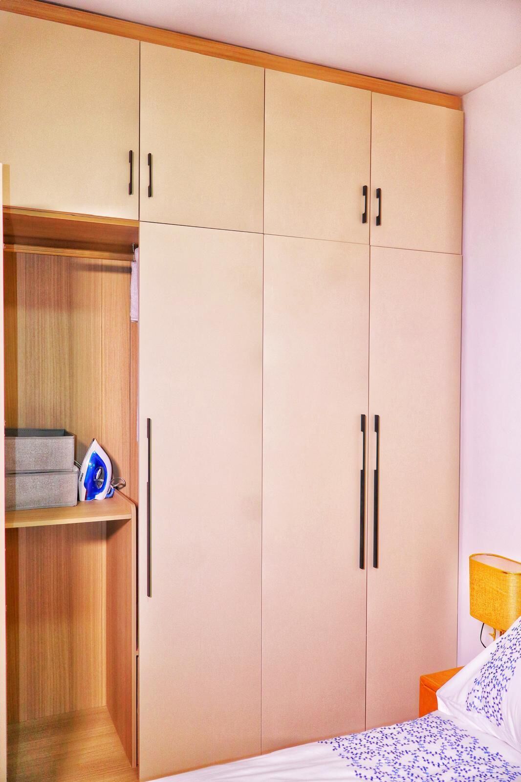Une chambre à coucher avec une grande armoire, un lit recouvert d’une couette à motifs et une table de chevet avec une lampe.