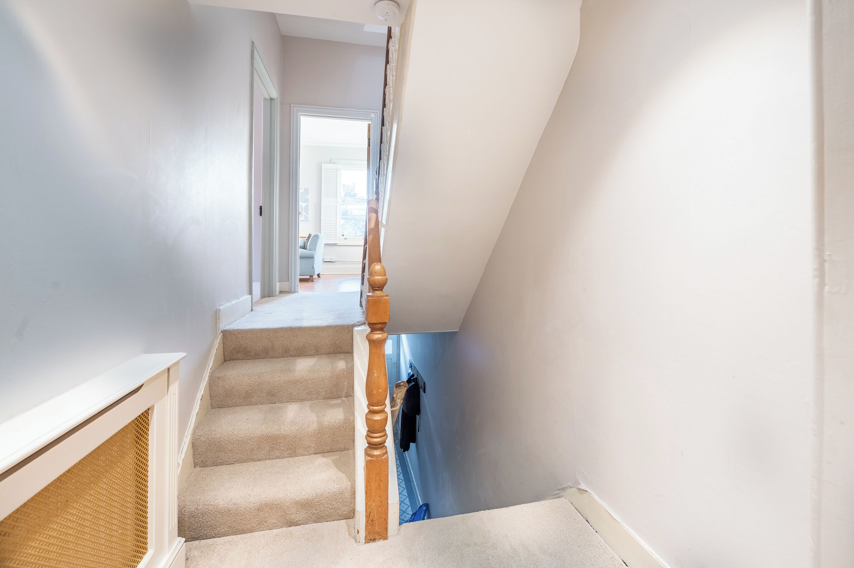 A staircase with beige carpeted steps, a wooden handrail, and a white wall.