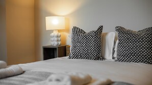 A neatly made bed with patterned pillows, a bedside lamp, and a small bedside table with a decorative object. - VESTO Three Bedroom Apartment in Clapham (London)