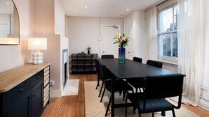 A modern dining area with a long table, black chairs, a wooden sideboard, a mirror, and a vase with flowers. - VESTO Three Bedroom Apartment in Clapham (London)