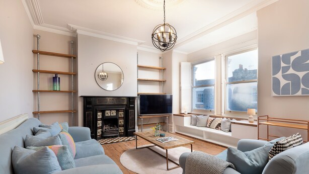 A modern living room with a fireplace, sofa, coffee table, and a large window with a city view. - VESTO Three Bedroom Apartment in Clapham (London)