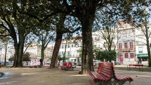 Un parque con bancos y árboles, una zona de juegos y edificios al fondo.