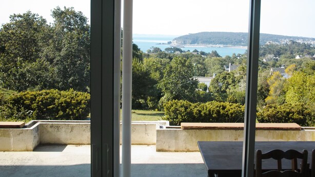 Una terraza con vistas a un paisaje costero, que incluye árboles, una colina y una masa de agua.