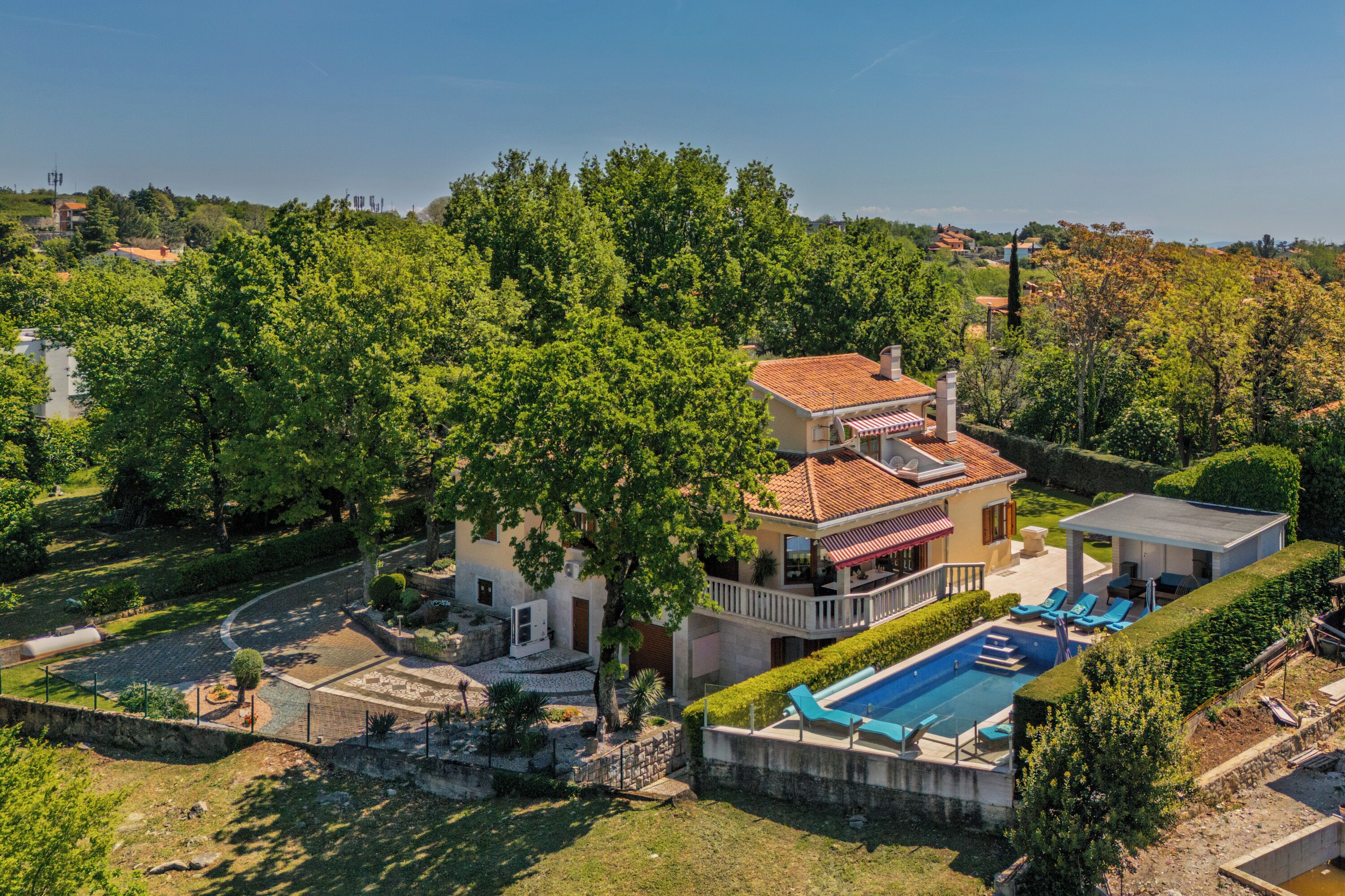 A two-story house with a swimming pool, surrounded by lush greenery and a clear sky.