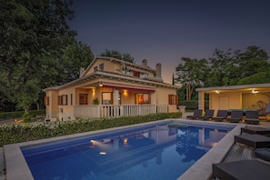A two-story house with a swimming pool, outdoor seating, and a well-maintained garden.