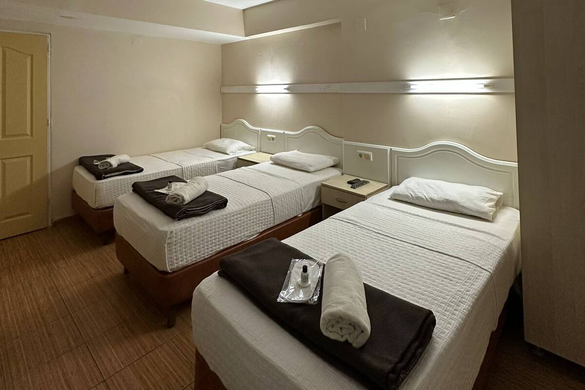 A hotel room with three single beds, a wooden floor, a door, and a light fixture on the ceiling.