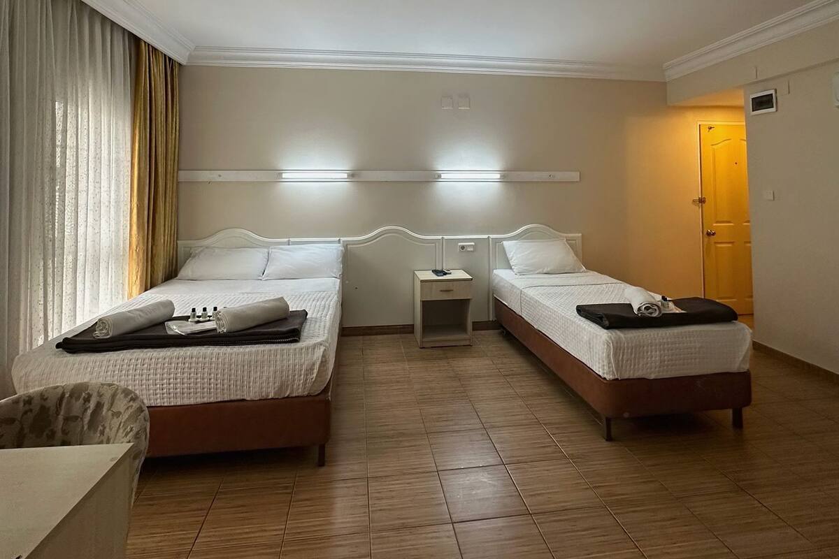 A hotel room with two beds, a small bedside table, a chair, and a door.