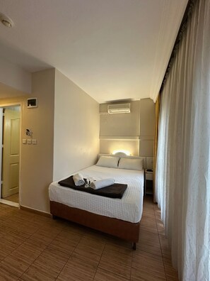 Hotellihuone, jossa on sänky, yöpöytä ja ilmastointilaite.