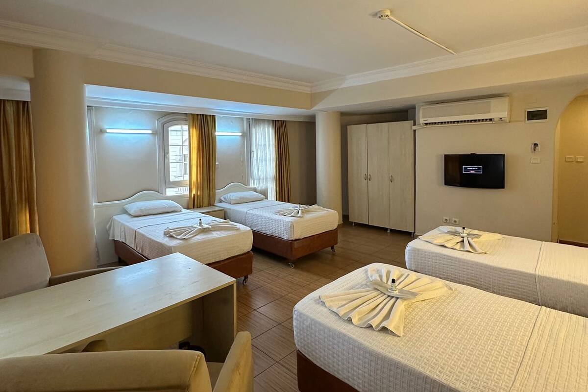 A hotel room with two single beds, a desk, a chair, a TV, and an air conditioning unit.