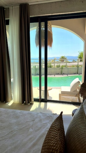 Ein Hotelzimmer mit einer großen Schiebetür zum Poolbereich, einem Bett mit weißer Bettwäsche und Blick auf Pool und Landschaft.
