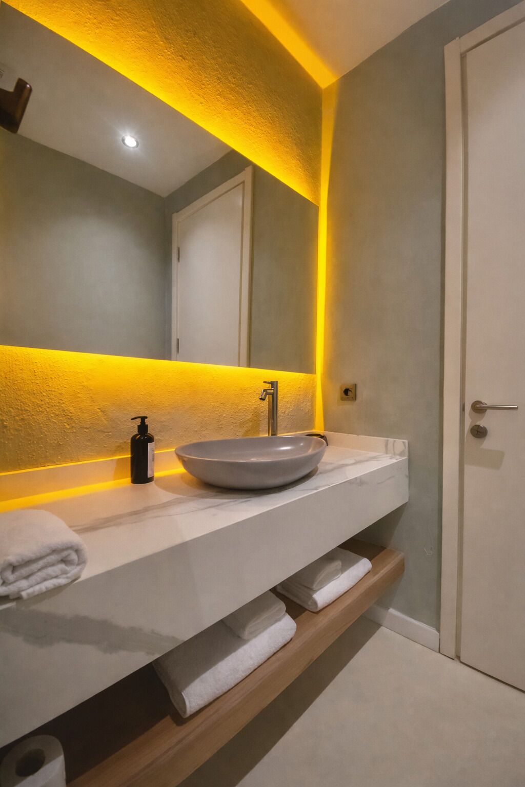 Un baño con un lavabo blanco, un espejo y una tira de luz amarilla.