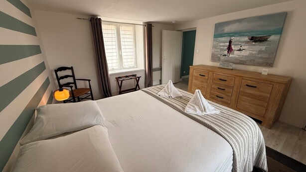 Een hotelkamer met een groot bed, een houten dressoir, een stoel, een bureau en een schilderij aan de muur.
