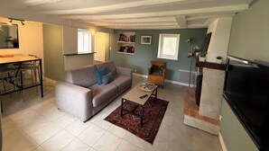 Een woonkamer met een bank, een salontafel, een eethoek met een tafel en stoelen, een televisie en een open haard.