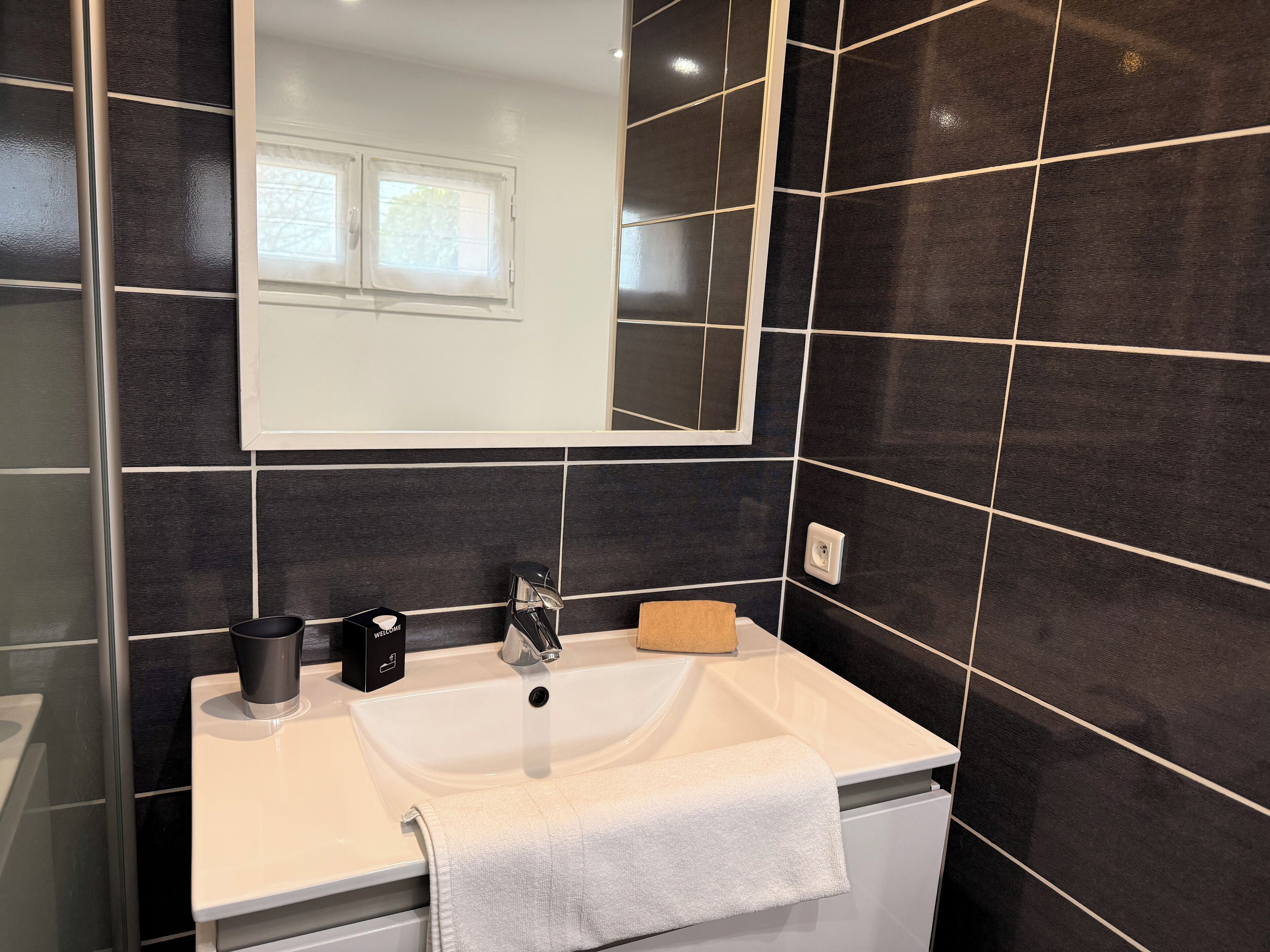 A bathroom with a white sink, a mirror, and black tiled walls.